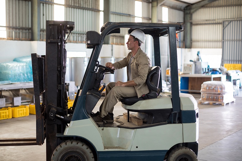 Worker driving forklift in oil factory